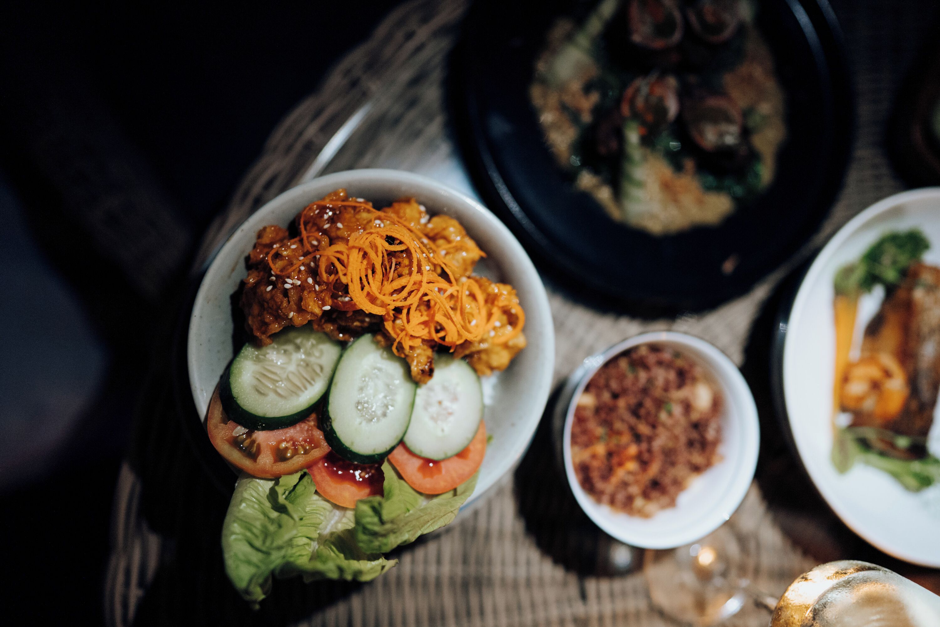 Uma refeição com diversos pratos, incluindo uma salada com pepinos, tomates e cenoura ralada, e um prato que parece ser de carne.