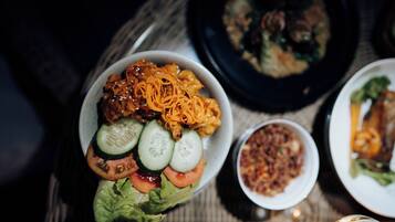 Uma refeição com diversos pratos, incluindo uma salada com pepinos, tomates e cenoura ralada, e um prato que parece ser de carne.
