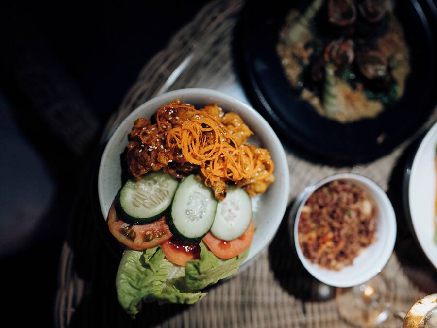 Uma refeição com diversos pratos, incluindo uma salada com pepinos, tomates e cenoura ralada, e um prato que parece ser de carne.