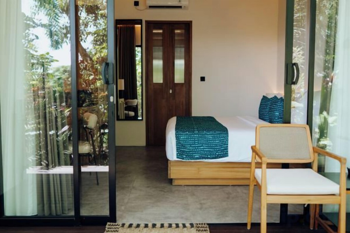 A bedroom with a bed, a chair, and a view through a glass door.