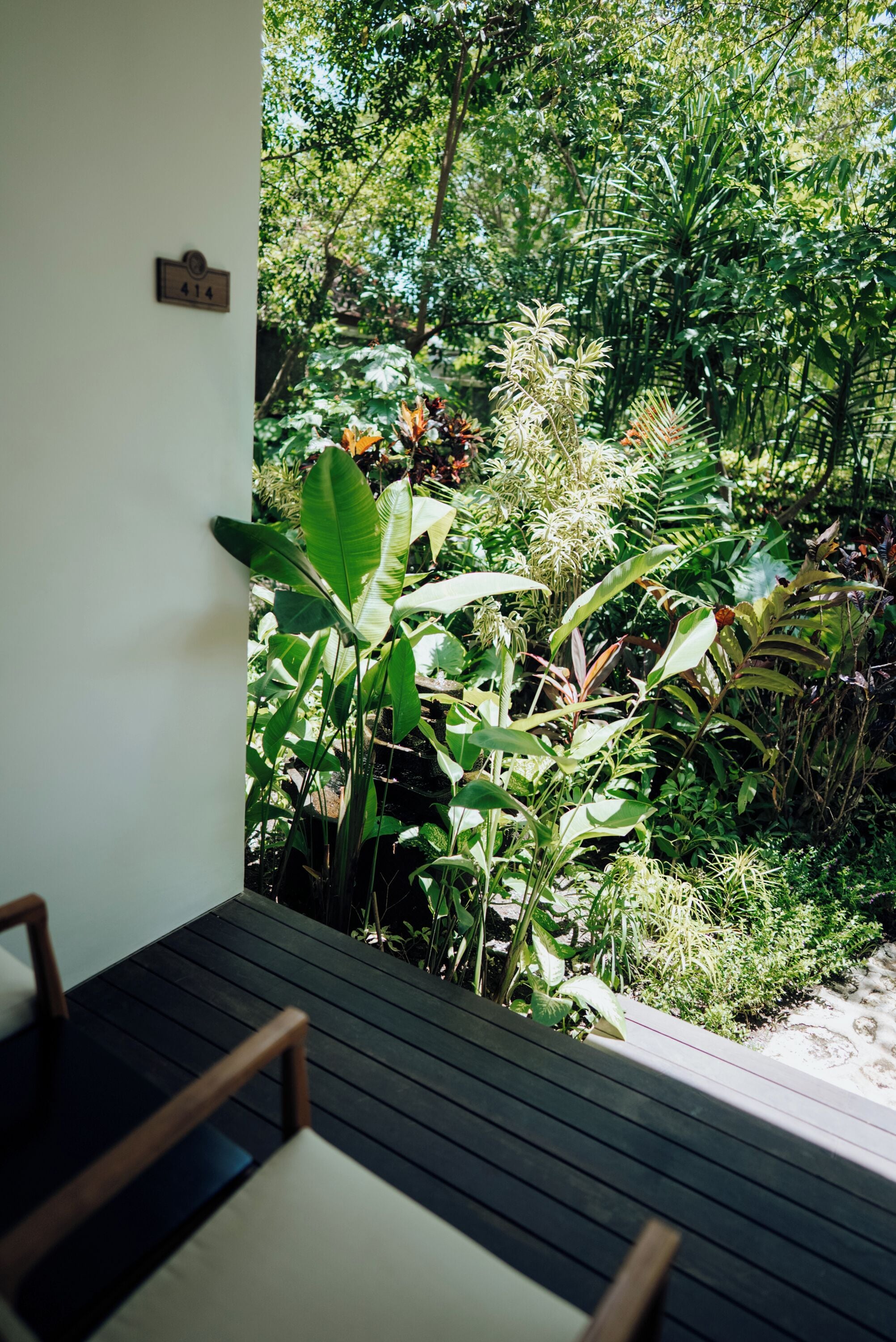 A wooden deck with a bench, surrounded by lush tropical plants and a wall-mounted sign.