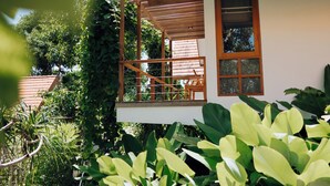 Una casa con techo rojo, un porche de madera y un jardín con hojas verdes grandes.