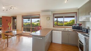 Eine moderne Küche mit Kochinsel, Geschirrspüler, Herd und Mikrowelle. Große Fenster bieten Blick ins Freie.