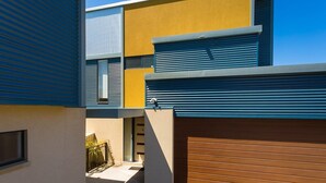Un bâtiment moderne dont les murs extérieurs sont peints dans des tons de bleu, de jaune et de brun, et qui est doté d'une porte de garage et d'une fenêtre.