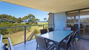 Un espace repas extérieur moderne, doté d’une table et de chaises en verre, offrant une vue panoramique sur un paysage pittoresque, avec des arbres et des collines.