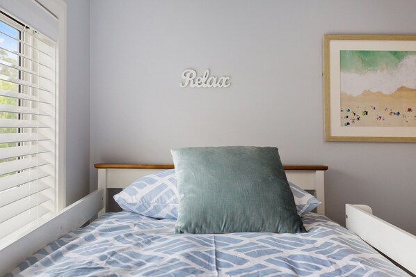 Un dormitorio con cama, almohada, una obra de arte en la pared y una ventana con persianas.
