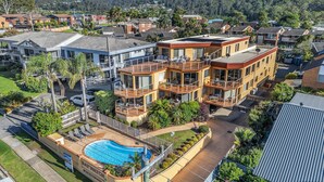 A multi-story residential building with a pool, balconies, and a view of a hilly area. - Baywatch Apartments Merimbula- 2 bedroom with beautiful views (Merimbula)