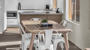 A modern kitchen with white cabinets, a wooden dining table, and white chairs. - Baywatch Apartments Merimbula- 2 bedroom with beautiful views (Merimbula)