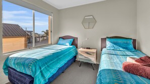 A hotel room with two beds, a nightstand, a lamp, and a view of the outside. - Baywatch Apartments Merimbula- 2 bedroom with beautiful views (Merimbula)