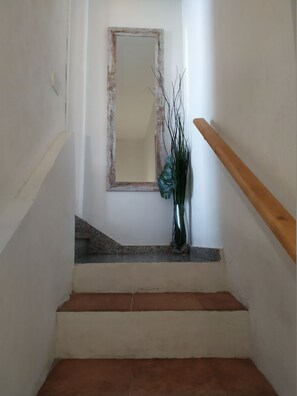 A staircase with a wooden handrail, a mirror on the wall, and a vase with branches on the landing.