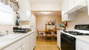 A compact kitchen with white cabinets, a wooden dining table, and a black stove. - San Pablo 30 nights or more (Seaside)