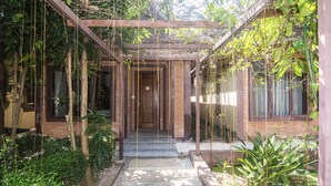 Un pasaje cubierto con un muro de ladrillo y vigas de madera, rodeado de abundante vegetación y plantas.