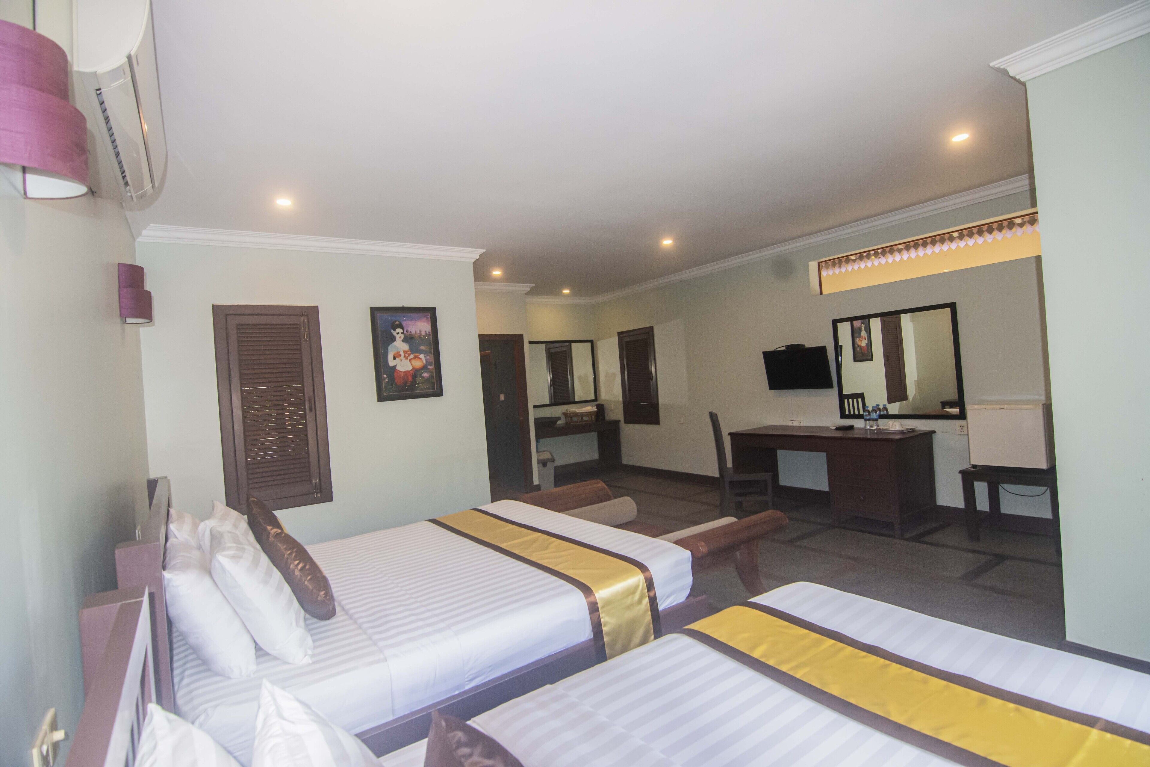 A hotel room with two beds, a desk, a chair, a mirror, and a small sitting area.