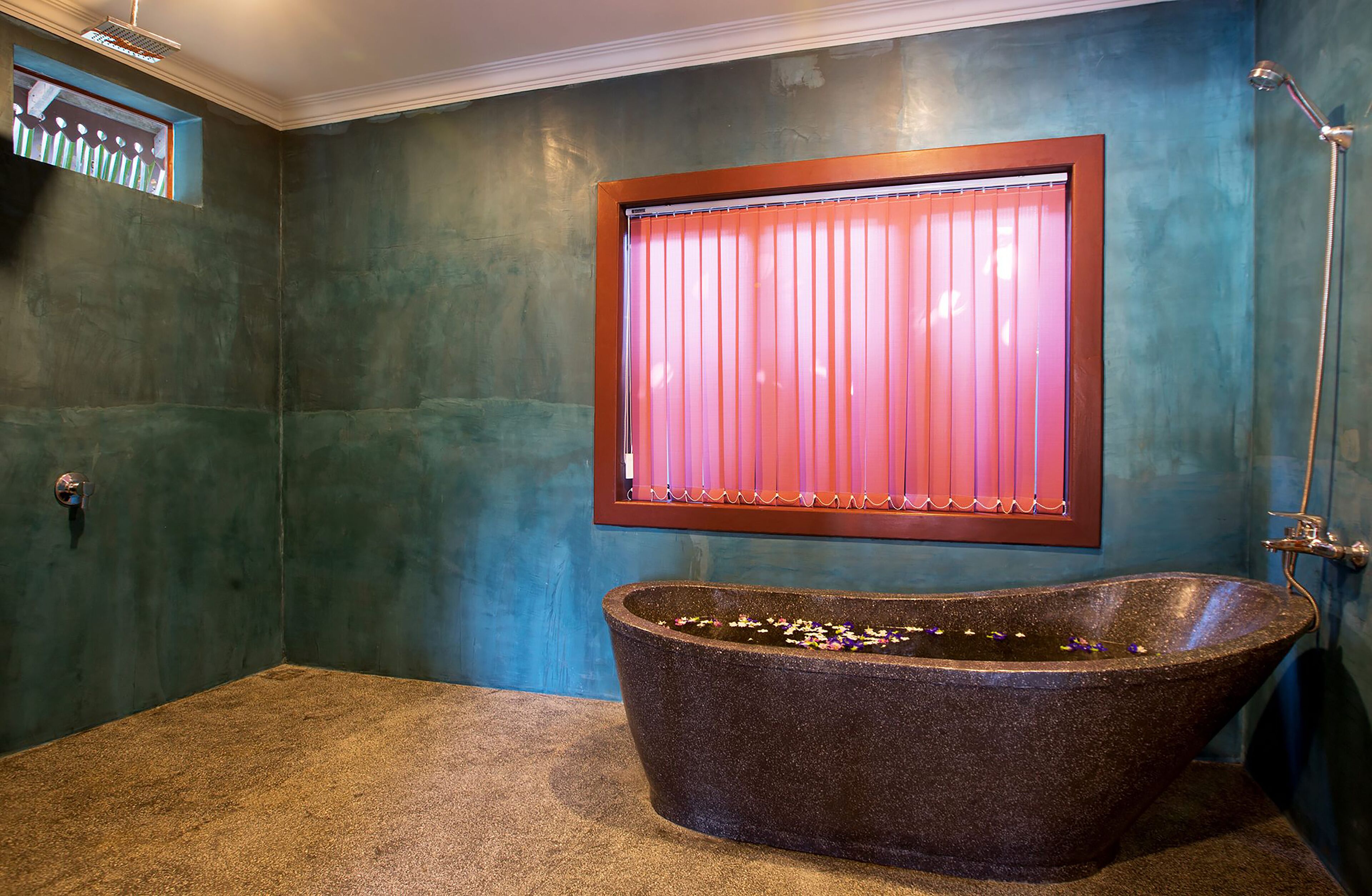 Un baño con una bañera de piedra independiente, una ventana con persianas rosadas y una zona de ducha.