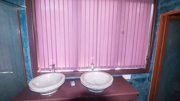 A bathroom with two stone sinks, a wooden vanity, and a window with pink blinds.