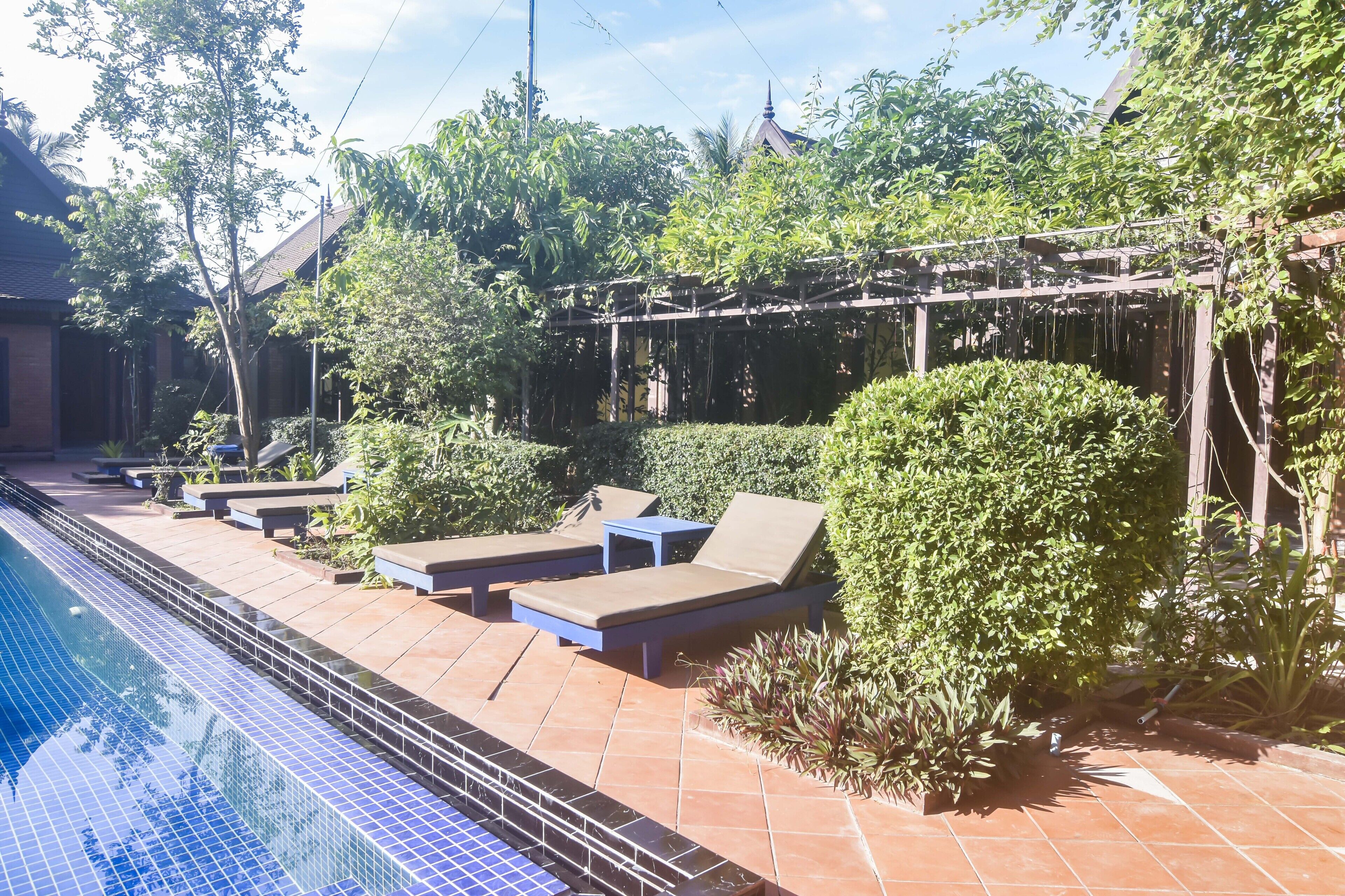 A swimming pool with tiled edges, lounge chairs, and a pergola with climbing plants.