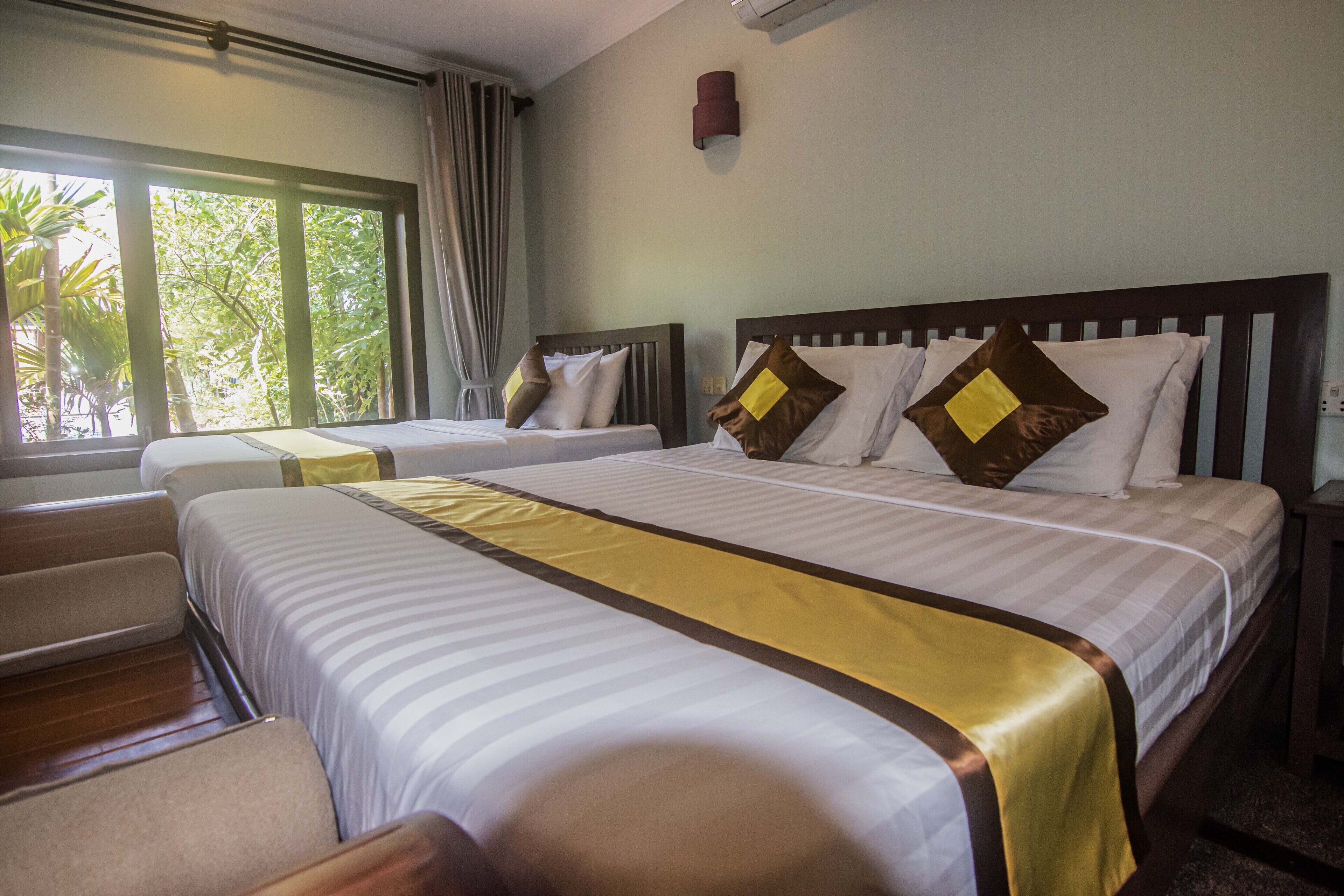 Quarto de hotel com duas camas, uma janela grande e vista para o verde lá fora.