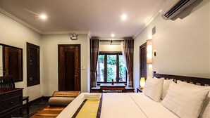 Habitación de hotel con una cama grande, muebles de madera, un escritorio y vistas a zonas verdes.
