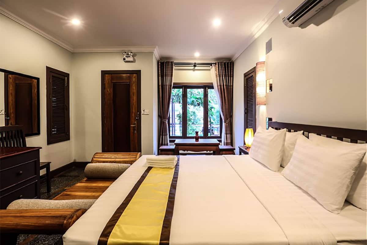 Quarto de hotel com uma cama grande, mobiliário de madeira, uma mesa de escritório e vista para o verde lá fora.