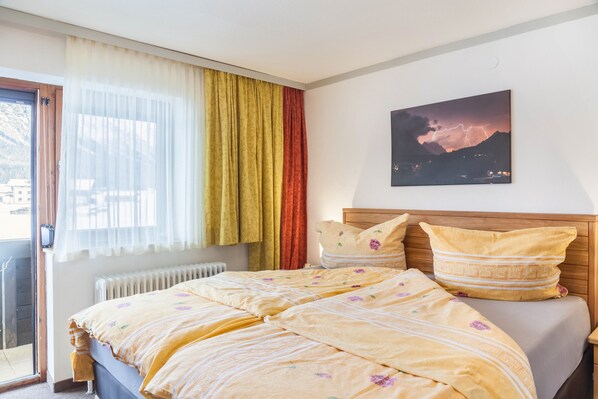 Un dormitorio con cama, cortinas, un radiador y un cuadro en la pared.