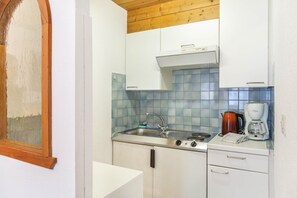 Une cuisine avec des meubles blancs, un plan de travail carrelé, une cuisinière, un évier et une machine à café.