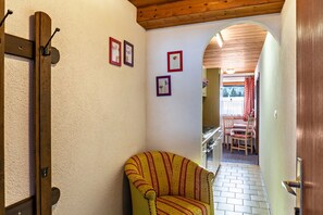 Un couloir étroit avec une porte en bois, un fauteuil à rayures et un coin repas comprenant une table et des chaises.