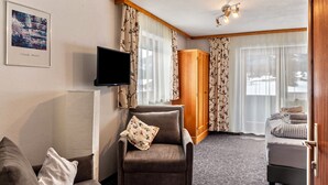 Ett hotellrum med en soffa, fåtölj, tv, ett träskåp och en säng med ett rutigt överkast.