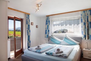 A bedroom with a bed, a nightstand, a window with curtains, and a view of a garden.