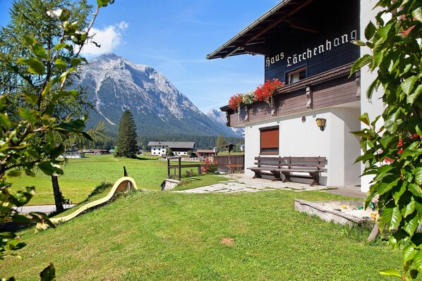 A building with a sign reading 'Haus Lärchenhang' in a grassy area with a mountain in the background.