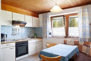 A kitchen with wooden cabinets, a stove, a sink, and a window with curtains.