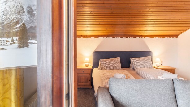 Un dormitorio con techo de madera, una cama con ropa de cama a cuadros, dos lámparas de noche y una mesita.
