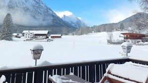 Un paisaje montañoso cubierto de nieve con cielo despejado, una terraza de madera y un edificio con tejado nevado.