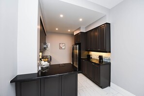 Kitchen features a stainless steel refrigerator, coffee maker, and sink on a small island with a tile floor.