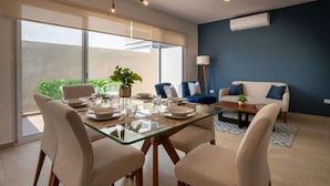 Un salon moderne avec une table à manger en verre, des chaises beige, un canapé bleu et une table basse.