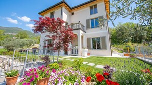 Ein zweistöckiges Haus mit Balkon, einem blühenden Garten und Blick auf die Landschaft.