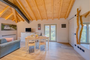 Un interior moderno con techo de madera, zona de comedor, sofá, televisor y ventana con vistas.
