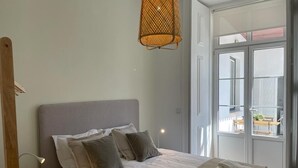 Une chambre à coucher avec un lit, des oreillers, une lampe de chevet, un luminaire suspendu et une vue sur le balcon extérieur.