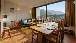 A dining area with a large table set for four, wooden chairs, a sofa, and a view of mountains through large windows. - La Maison De Montroc Family-Holidays w/4BR, + Fireplace, Sleeps 8, Le Tour (Argentière), France (Le Tour (Argentière))