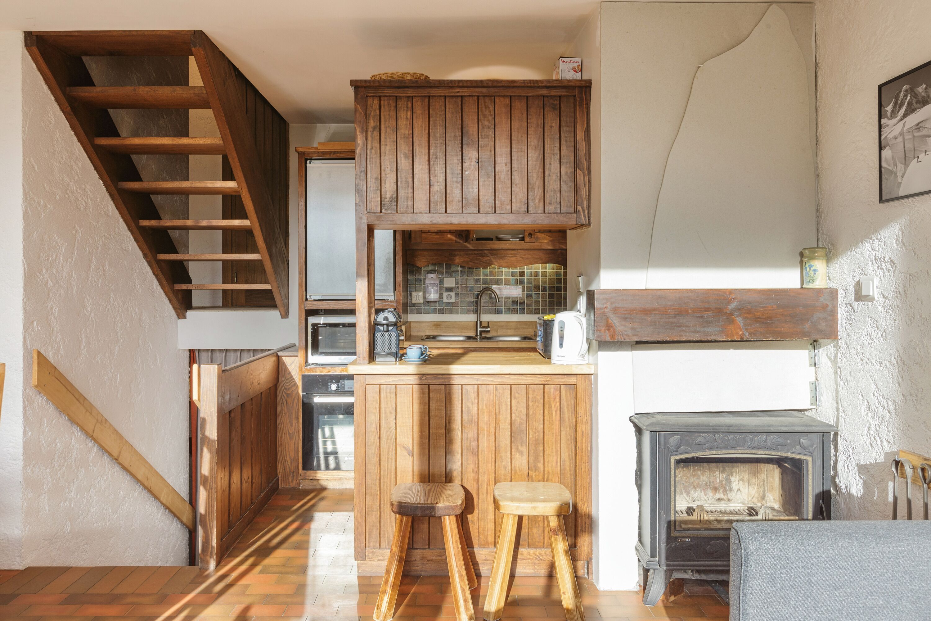 Une cuisine avec des meubles de rangement en bois, une cuisinière encastrée et un escalier en bois.