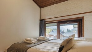 A bedroom with a bed, a window with a view of buildings and mountains, and a wooden ceiling. - La Maison De Montroc Family-Holidays w/4BR, + Fireplace, Sleeps 8, Le Tour (Argentière), France (Le Tour (Argentière))
