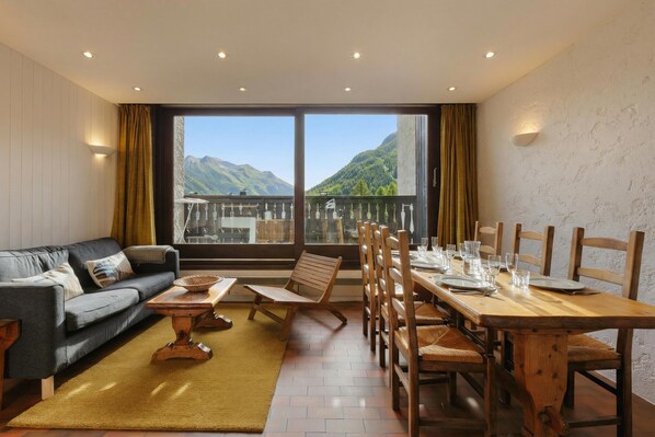Una habitación con sofá, mesa de comedor, sillas y vistas a montañas a través de amplias ventanas.