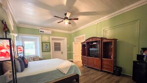 Un dormitorio con una cama, ventilador de techo, un armario de madera y un televisor.