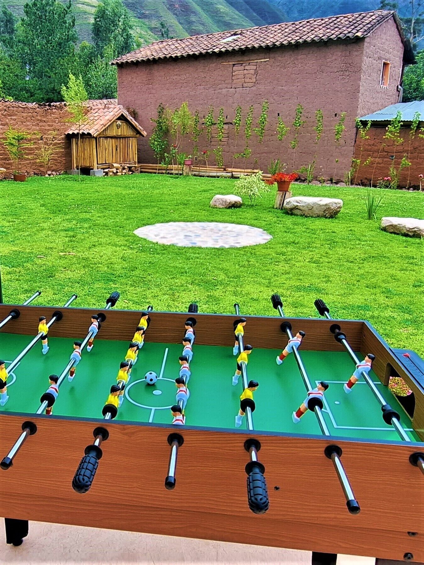 A foosball table in a grassy yard with a rustic building in the background.
