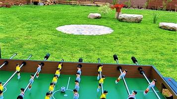 A foosball table in a grassy yard with a rustic building in the background.