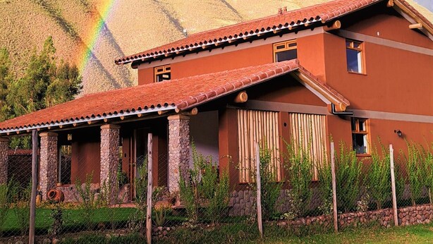 A house with a red-tiled roof, stone pillars, and a mountainous backdrop. - Kallpawasi, Andean House in the Sacred Valley of the Incas. Service and Nature. (Urubamba)