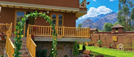 A two-story house with a wooden balcony, a stone staircase, and a well-maintained garden with outdoor furniture.