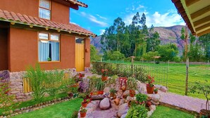 A house with a tiled roof, a stone wall, and a garden with potted plants and a stone pathway. - Kallpawasi, Andean House in the Sacred Valley of the Incas. Service and Nature. (Urubamba)