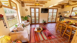A cozy living room with a sofa, coffee table, and a dining area with wooden chairs and a table. - Kallpawasi, Andean House in the Sacred Valley of the Incas. Service and Nature. (Urubamba)
