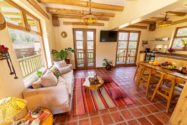 A cozy living room with a sofa, coffee table, and a dining area with wooden chairs and a table. - Kallpawasi, an Andean house in the Sacred Valley of the Incas. Service and Nature. (Urubamba)