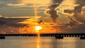 A sunset over a body of water with a pier extending into the water. - VERY Spacious 3rd floor unit with gorgeous ocean view and wrap around porch (Frederiksted)